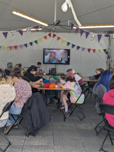 picture of a number of people sitting at tables in a tent doing crochet